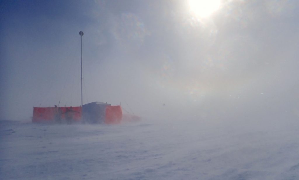 A photo of the Sherman Island drilling set-up in tough blown-snow conditions with the sun peering through the gloom.