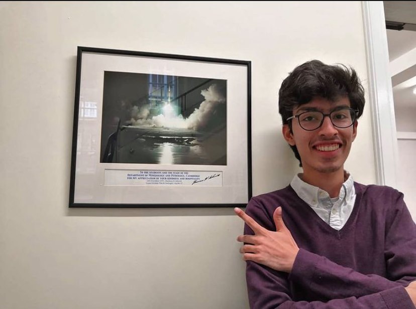 Image of Hassan smiling and standing in front of a photo of Apollo 17 launching