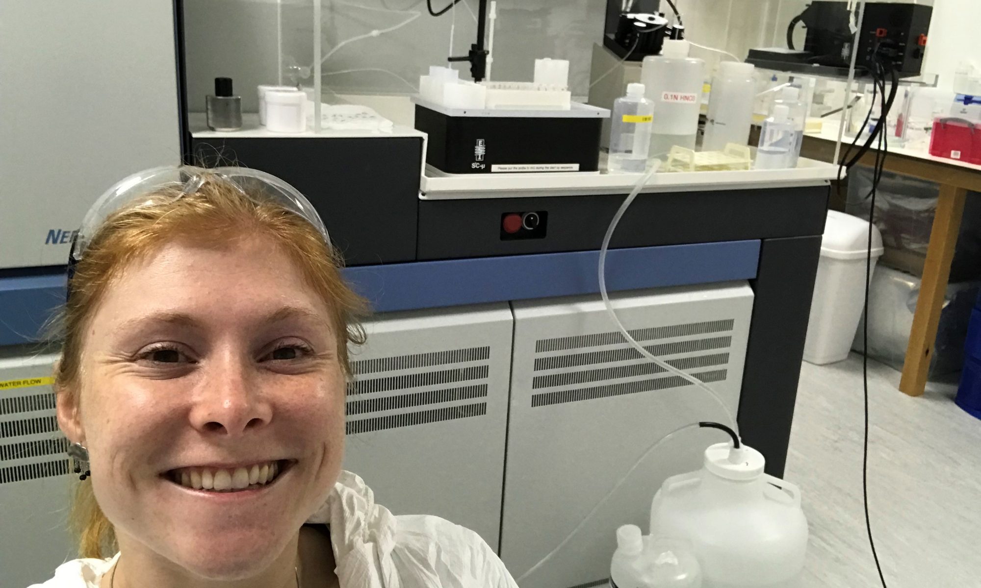 Carrie in the lab, wearing protective gear and stood in front of a mass spectrometer